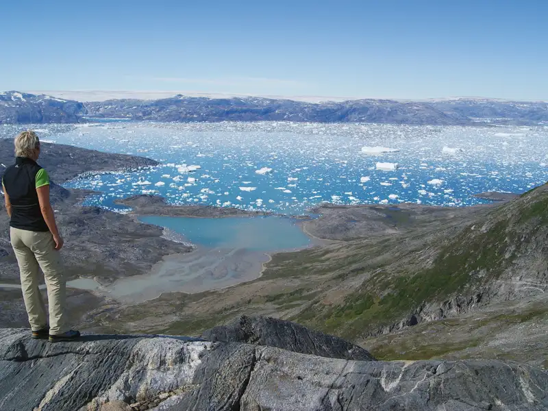 Wandergruppe pausiert auf einem Felsvorsprung und betrachtet die verschneiten Berge und die arktische Landschaft.